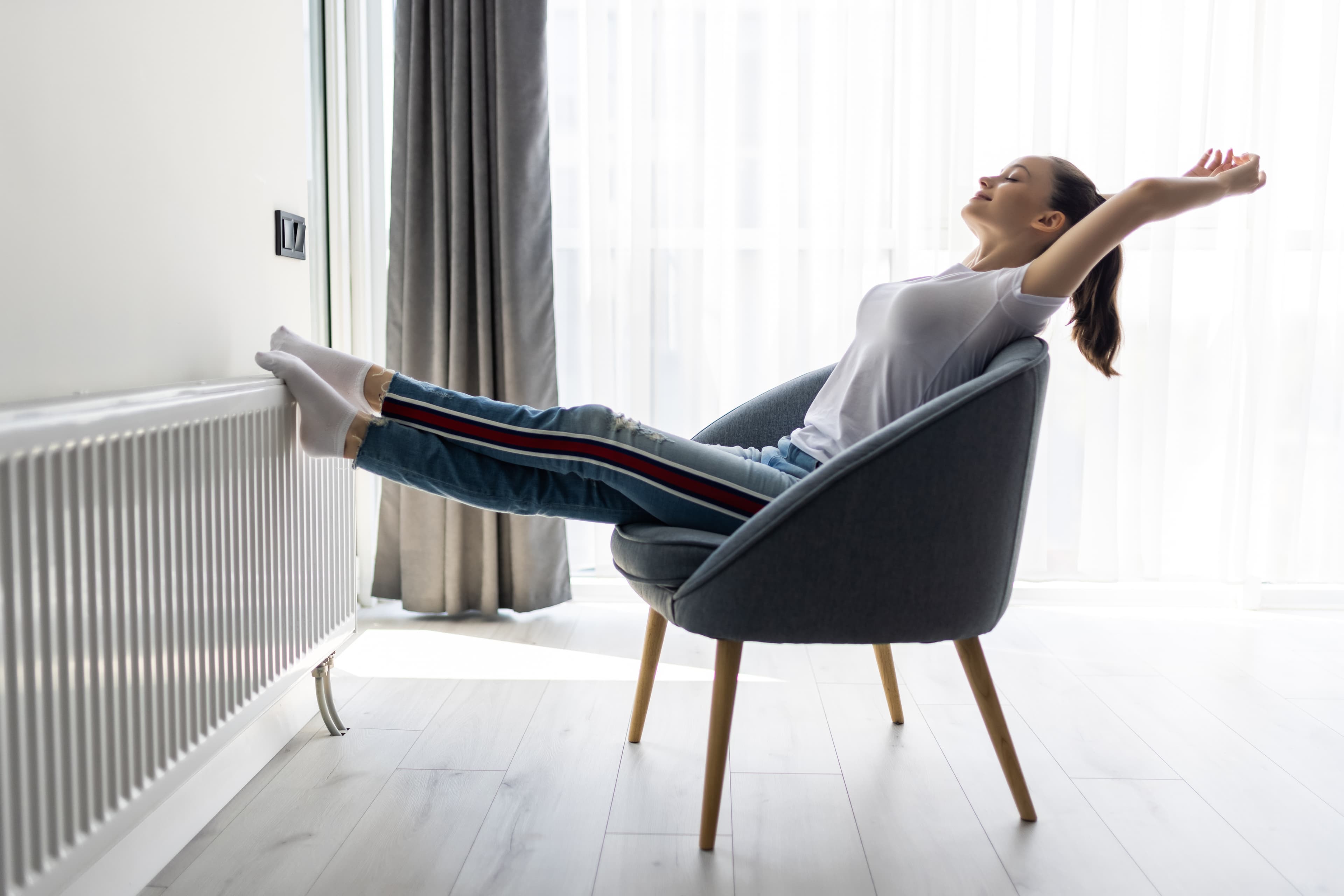 Mujer relajada en el salón de su casa, con un aire y una temperatura agradables junto a la ventana