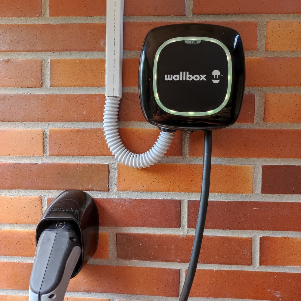 Cargador wallbox negro instalado en la pared de un garaje, con el conector en su soporte